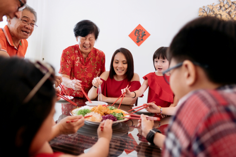 Family around the table doing the yee sang toss for Chinese New Year
